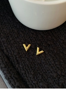 Macro detail of gold-toned V-shaped stud earrings on black fabric background