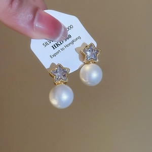 Detail of star-shaped stud earring with zircon inlay and hanging round white pearl