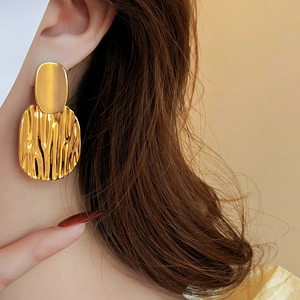 Vue détaillée de grandes boucles d'oreilles dorées géométriques à texture brossée