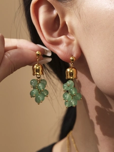 Dettaglio di orecchini a forma di uva con perle verdi e placcatura in oro 18k su modella