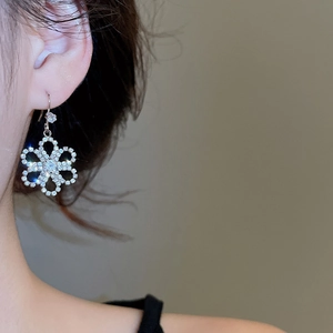 Detailed close-up of a silver flower earring with sparkling rhinestones on a female model