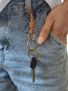 Close-up of brown leather cord keychain with brass horseshoe buckle on denim belt loop