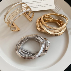 Detail of layered gold cuff bracelet and mixed metal snake chains on white ceramic tray