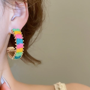 Detail view of woven C-shape hoop earrings with colorful knitting and gold metallic beads