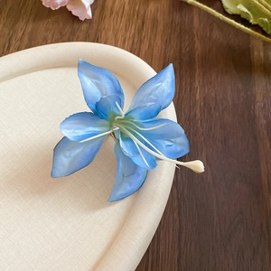 Detailed view of a blue silk hibiscus hair clip with white stamens on a beige tray