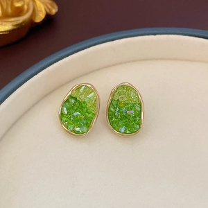 Detailed shot of irregular oval gold earrings with green gradient crystal on jewelry tray