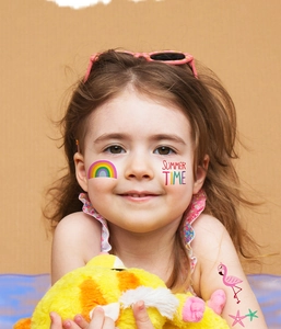 Dettaglio di tatuaggi estivi impermeabili con fenicottero e arcobaleno sul viso di bimba