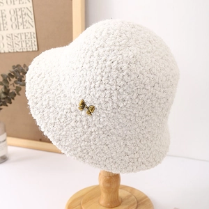 Close-up of white plush bucket hat with delicate golden bow metal accent on wooden stand