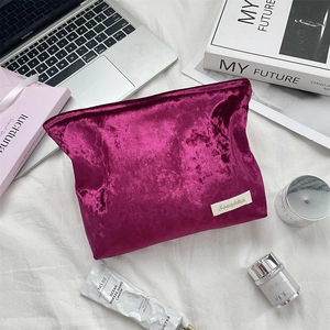 Flat lay of purple velvet cosmetic bag with zipper and logo label on a white bed