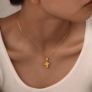 Detailed view of a gold cross pendant necklace worn on a white ribbed tank top