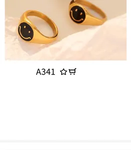 Close-up of dual gold rings featuring black enamel smiley faces on textured white paper