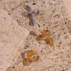 Detail of fluid cross ear clips in gold and silver finish on natural stone background