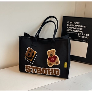 Close-up of black canvas tote bag featuring premium teddy bear towel embroidery detail
