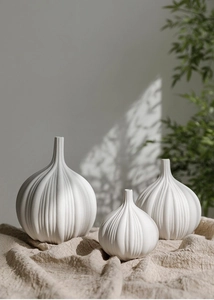 Dettaglio di tre vasi in ceramica bianca opaca a forma di aglio con texture a coste