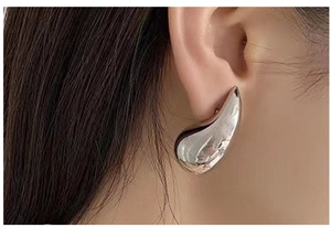 Close-up of a silver chunky teardrop earring on model showing sleek metallic finish