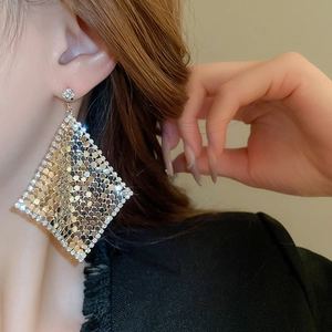 Macro shot of diamond-encrusted rhombic sequin drop earrings on a female model