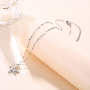 Detail of silver starfish pendant with sparkling zircon on a beige cylindrical display stand