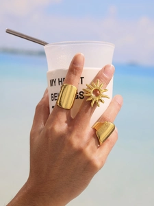 Close-up of golden wavy open rings and sunflower ring worn on fingers at the beach
