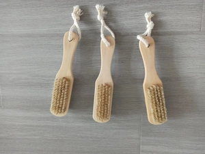 Three wooden body brushes with natural bristles and white cotton hanging ropes on gray wood