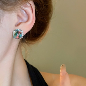Close-up of rainbow crystal stud earrings with clear diamond halo on a model's ear