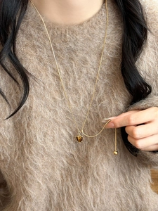 Detail of adjustable gold necklace with heart-shaped tiger eye stone on brown sweater