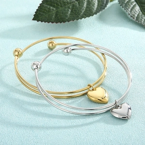Detailed view of gold and silver layered wire bracelets with heart pendants on leaf