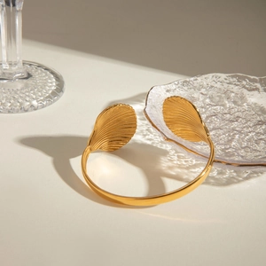 Macro detail of gold-plated bangle with textured scallop shells and adjustable opening