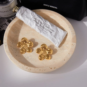 Elegante goldene Blumenohrringe aus Titanstahl auf einem Marmortablett mit Accessoires