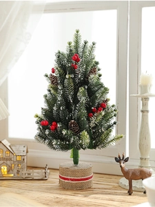 Close-up of mini snowy Christmas tree with red berries and burlap base on a wooden sill