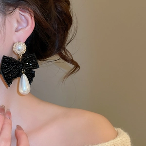 Close-up of vintage bow pearl drop earring with gold base and white teardrop pearl
