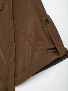 Détail de la manchette de chemise safari avec bouton en métal et tissu marron texturé