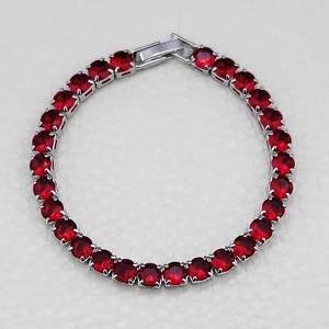 Macro detail of red round-cut zircon tennis bracelet with silver metal and fold-over clasp