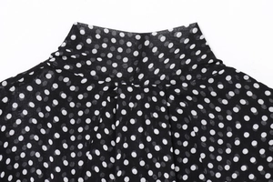 Detail of the standing collar and pleated texture on the black and white polka dot shirt