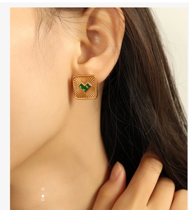 Close-up of model wearing gold square stud earrings with green radiant gemstones