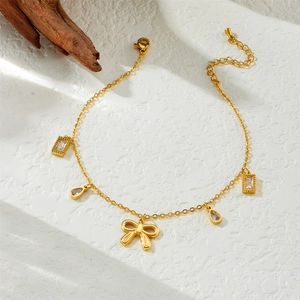 Gold stainless steel anklet with bow pendant and teardrop cubic zirconia on textured background