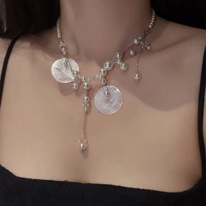 Detail of silver tassel necklace with white pearls and round shell pendants on the collarbone