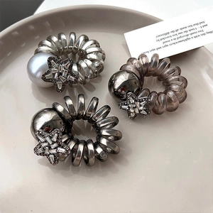 Detail of three spiral hair ties with rhinestone stars, metallic spheres, and pearls