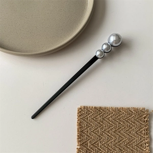 Close-up of minimalist black hair pin with three gradient silver-grey pearls on fabric