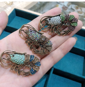 Detailed view of three vintage rhinestone lobster brooches held in hand with colorful crystals