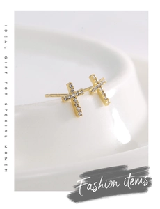 Detail of gold cross stud earrings with sparkling zircons on a white ceramic stand