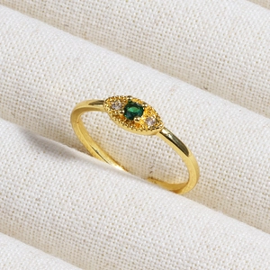 Detail of a gold emerald ring with a minimalist eye-shaped design and side zircon accents