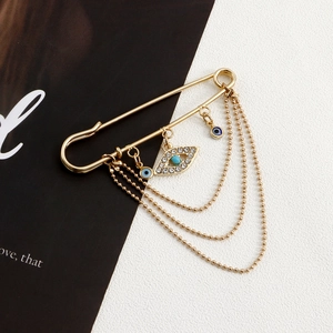 Detailed view of gold-tone evil eye brooch with multilayered tassels on a magazine