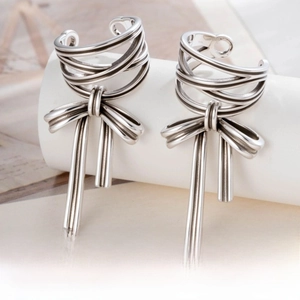 Detailed macro view of silver bow-knot ear clips with dangling cylindrical pendants