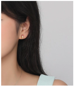 Detail of an ice cream cone stud earring with red zircon and golden texture on ear
