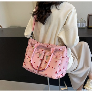 Detail of pink nylon tote bag with cherry print and multi-zipper pockets shown on model