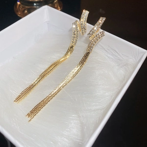 Macro shot of long gold tassel earrings with spiral crystal stud in a white jewelry box