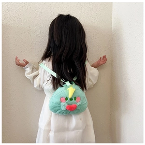 Detail view of a green plush dinosaur backpack with yellow horns on a young girl's back
