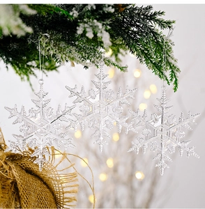 Three transparent acrylic snowflake ornaments hanging on a Christmas tree with warm bokeh light