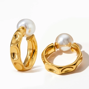 Detail showing gold C-shaped textured hoop earrings with large white pearls on white background