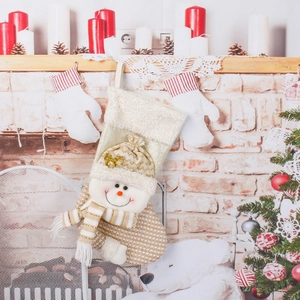 Knitted Christmas stocking with plush snowman hanging on a decorated fireplace mantel